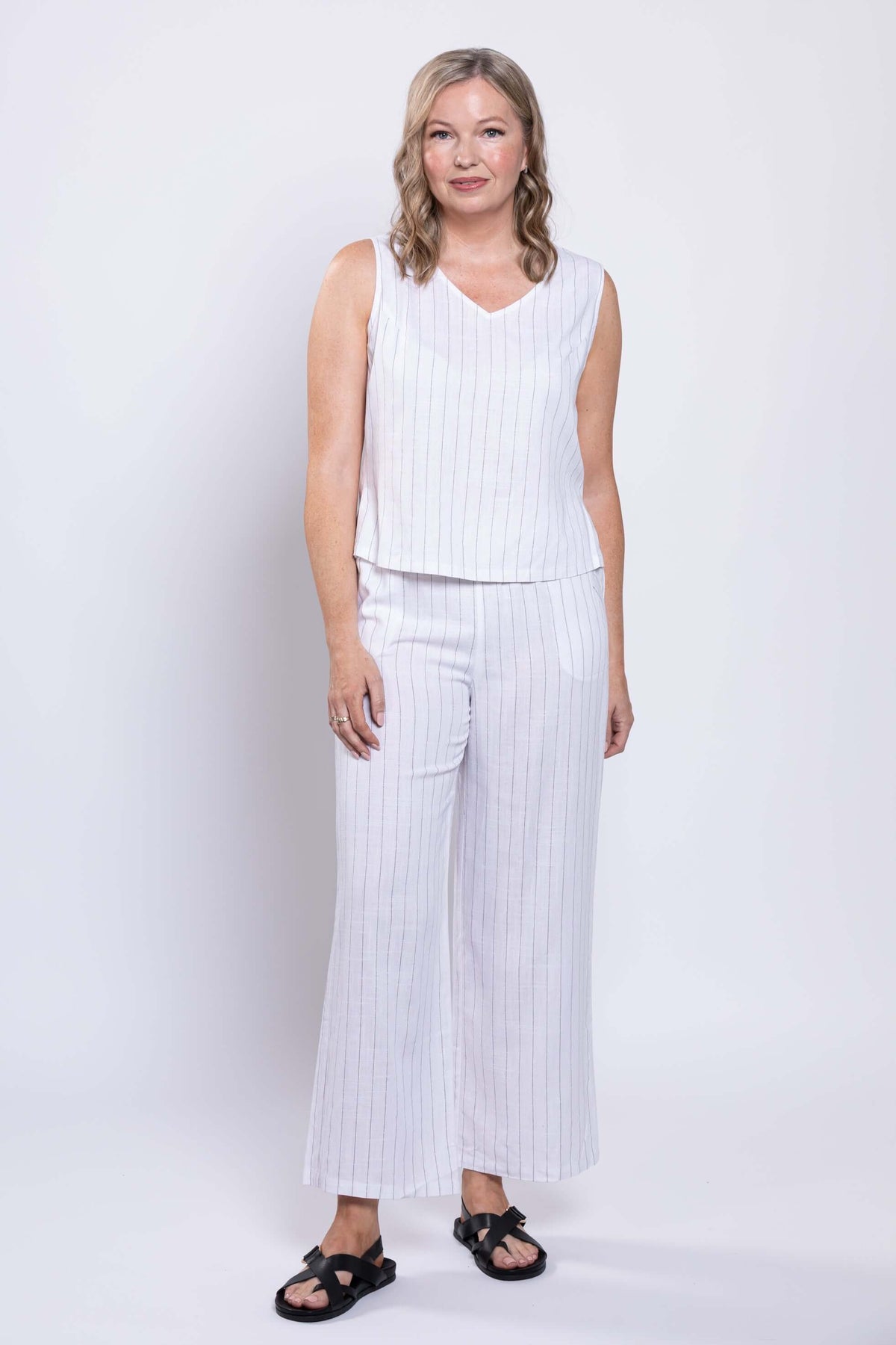 Woman in white pinstripe wide-leg pants and sleeveless top, standing front-facing