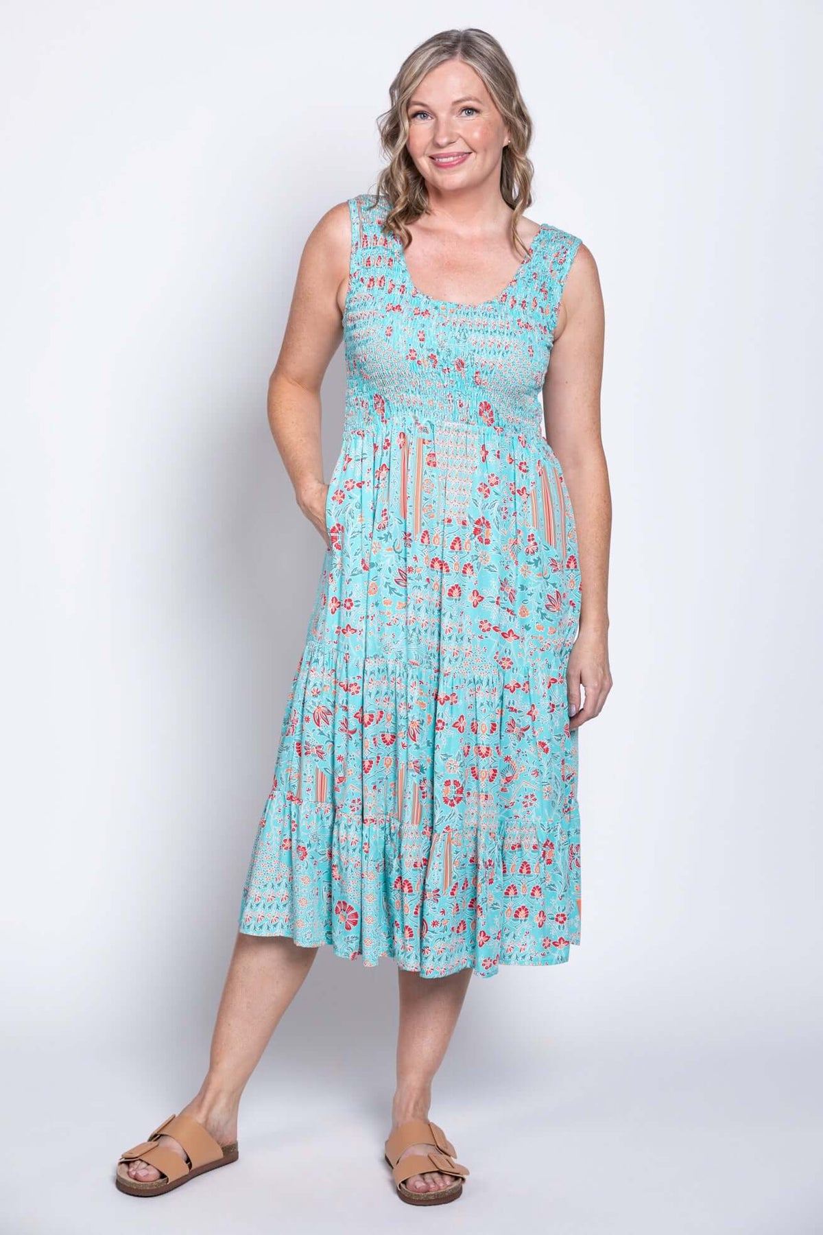 Woman standing in a blue floral print sleeveless midi dress with hands in pockets