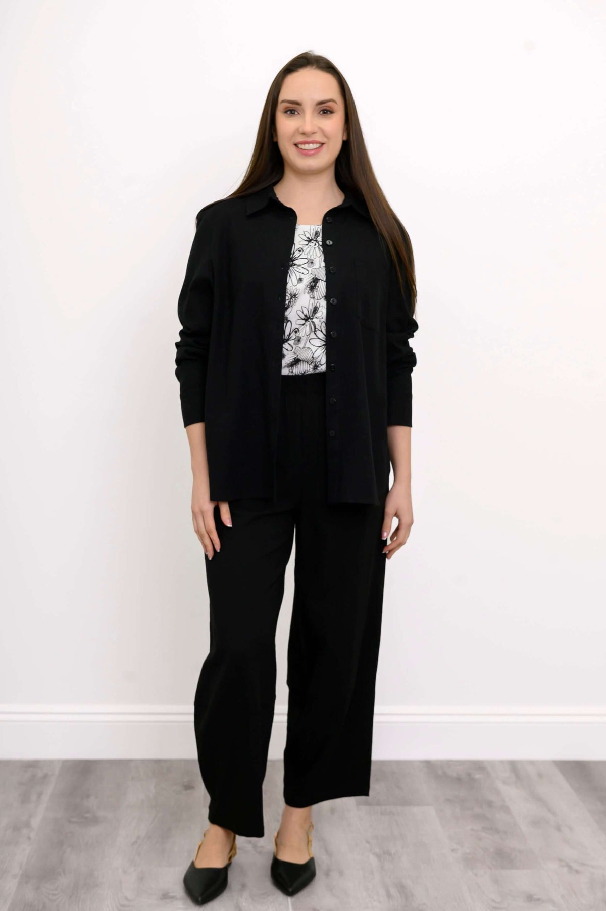 Woman standing in black wide-leg pants with floral printed top and black buttoned cardigan