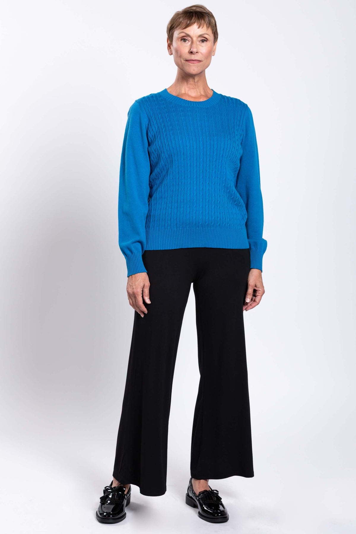 Woman standing in blue cable knit sweater, black pants, and black shoes