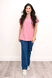 Woman standing in blush pink tee and blue jeans, facing forward