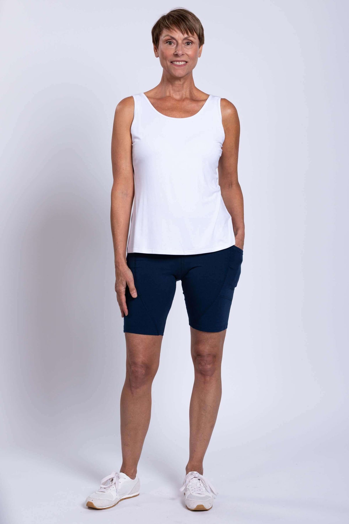 Woman standing in navy Robson Shorts and white sleeveless top, front view with hands in pockets