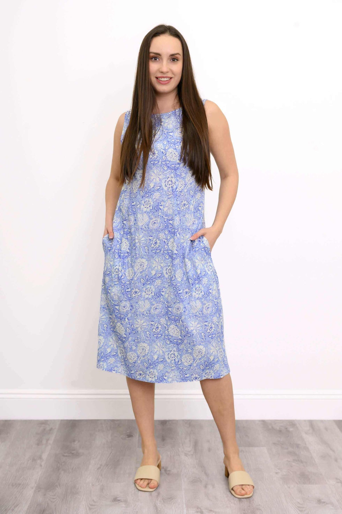 Woman standing with hands in pockets, wearing a light blue floral sleeveless dress