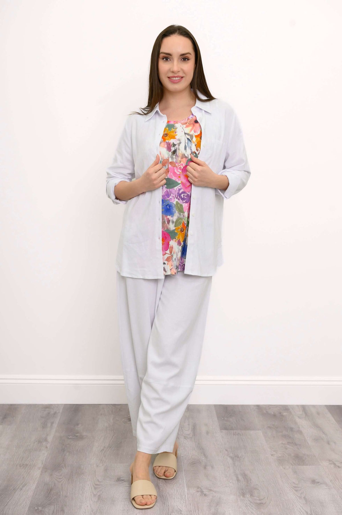 Woman in white pants and shirt, floral top underneath, standing straight