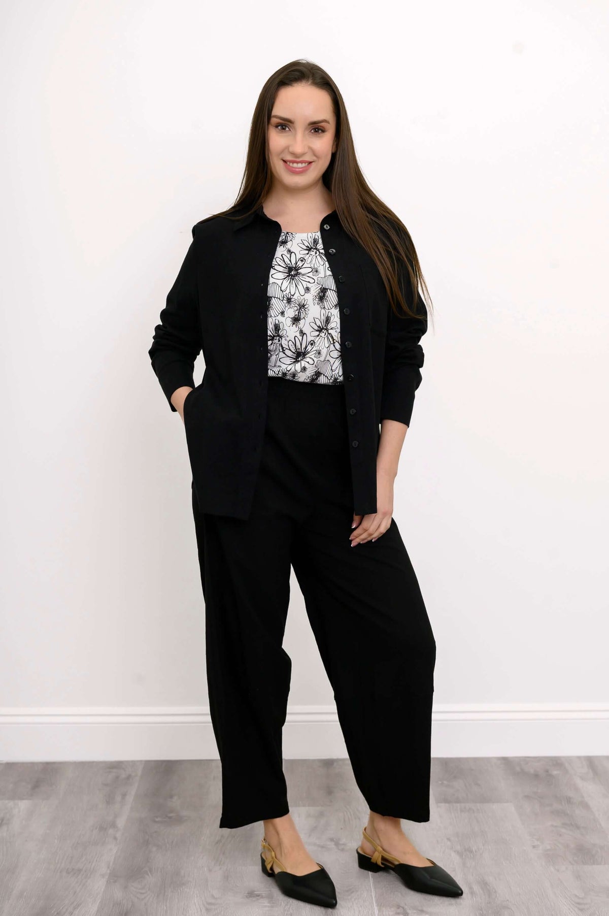 Front view of woman posing with her hand in her pocket wearing a black outfit on a floral print top