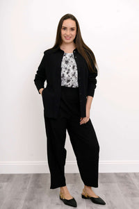 Front view of woman posing with her hand in her pocket wearing a black outfit on a floral print top