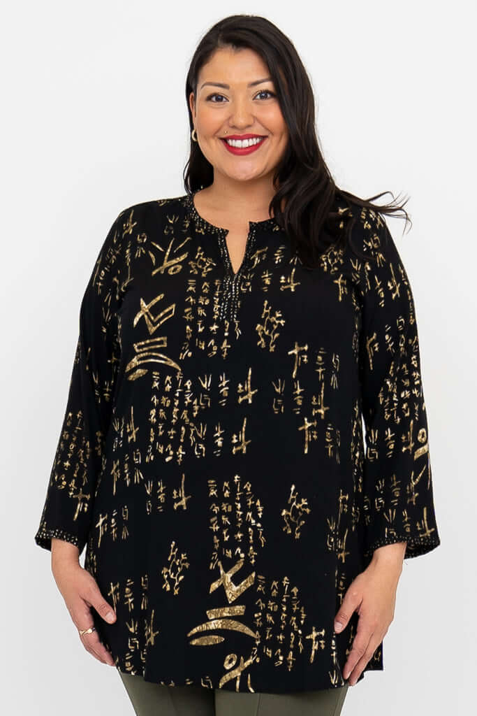 Woman wearing a black blouse with gold batik print, standing and smiling