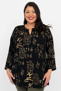 Woman wearing a black blouse with gold batik print, standing and smiling