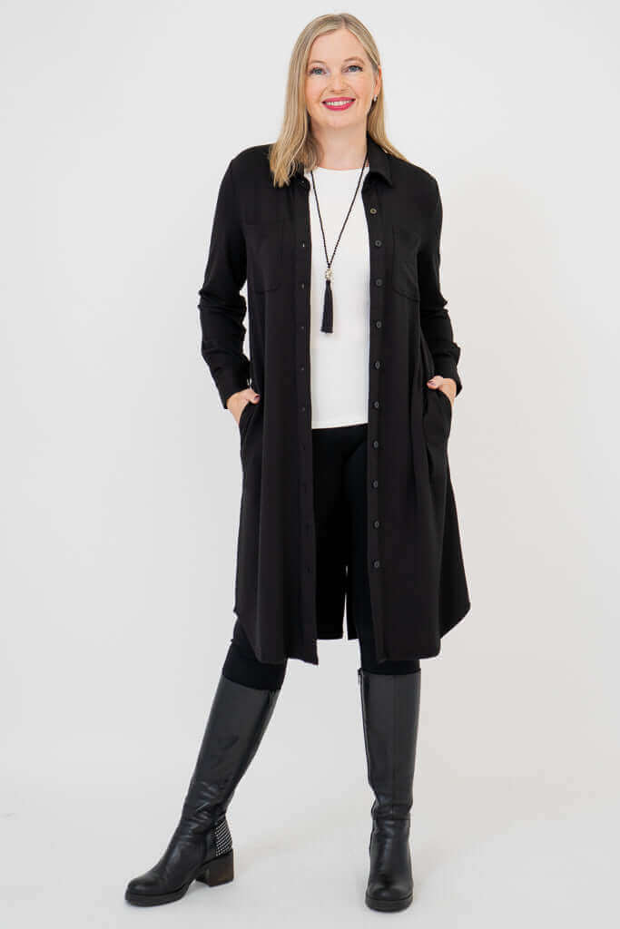 Woman wearing a long black button-down duster with side pockets, styled over white top and black boots
