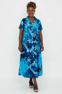 Woman wearing a blue batik short sleeve A-line button-up dress, standing and smiling