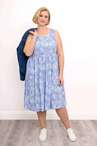 Woman wearing a blue floral tiered dress with white sneakers and holding a denim jacket
