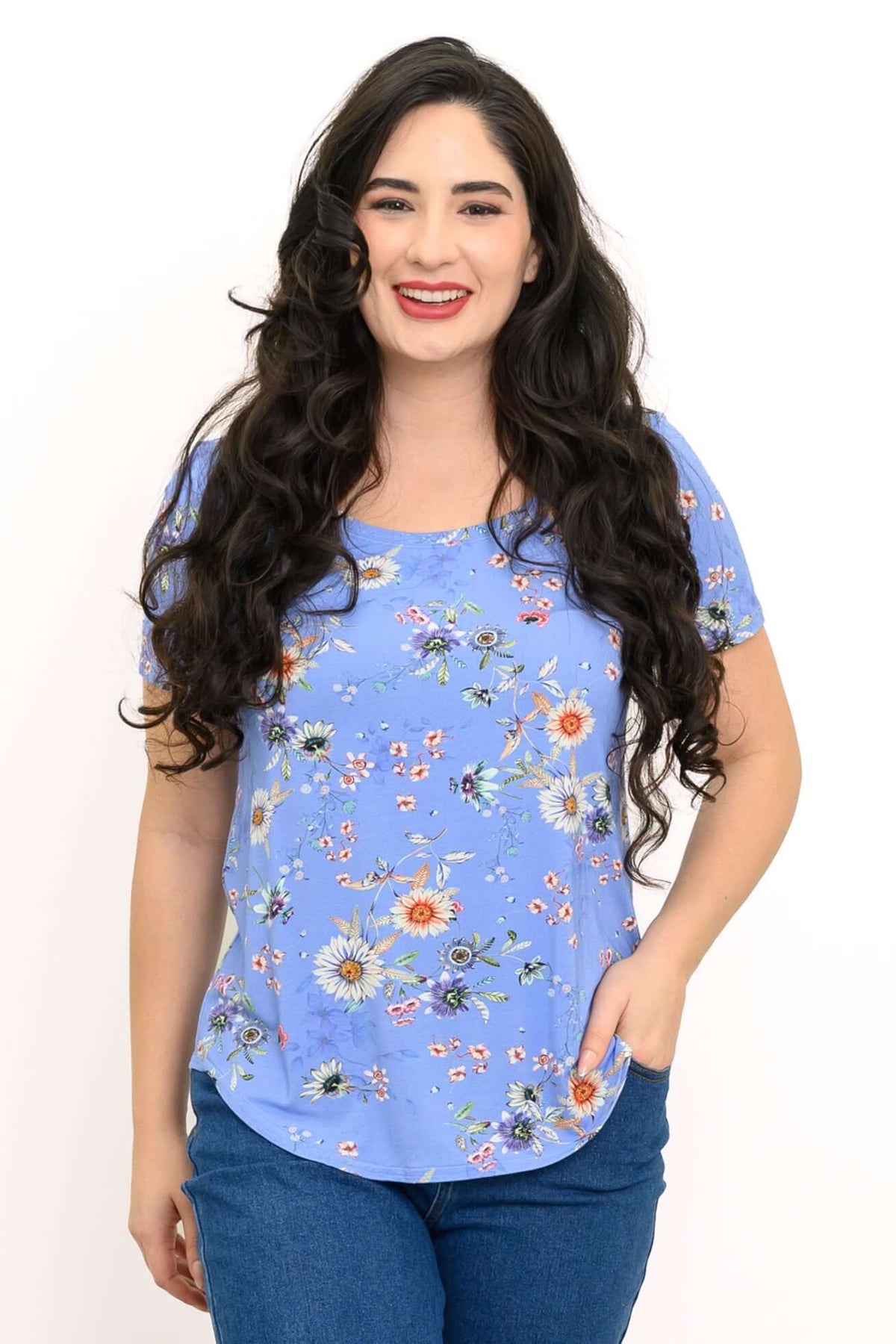 Woman wearing a blue short-sleeve floral tee with a rounded hem, facing forward and smiling