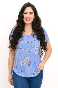 Woman wearing a blue short-sleeve floral tee with a rounded hem, facing forward and smiling