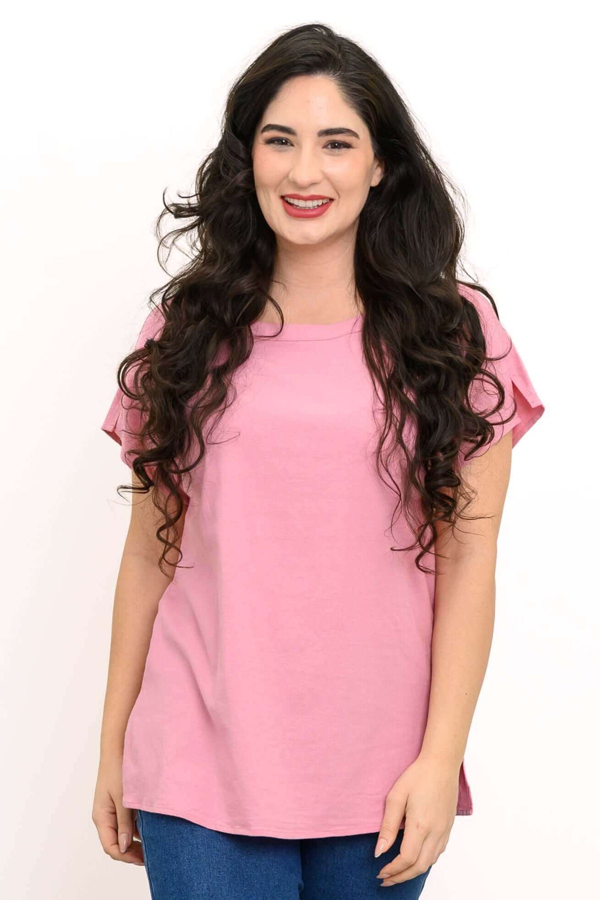 Woman wearing a blush pink tee with dolman cap sleeves and blue jeans, front view