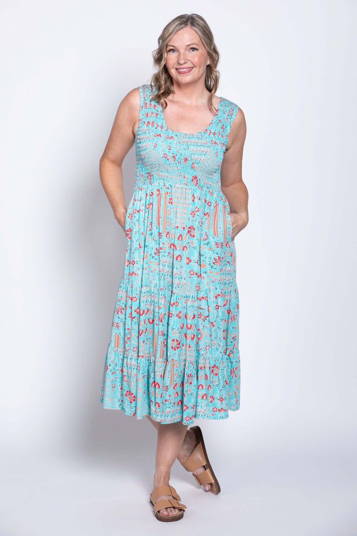 Woman wearing a light blue tiered sleeveless midi dress with red floral pattern, hands in pockets