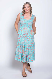 Woman wearing a light blue tiered sleeveless midi dress with red floral pattern, hands in pockets