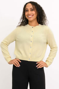 Woman wearing a light yellow cashmere cardigan with buttons, hands on hips