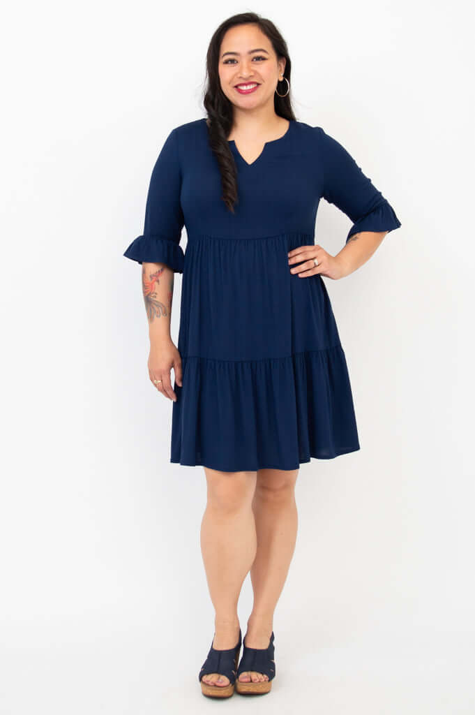 Woman wearing a navy tiered dress with ruffled sleeves, standing and smiling
