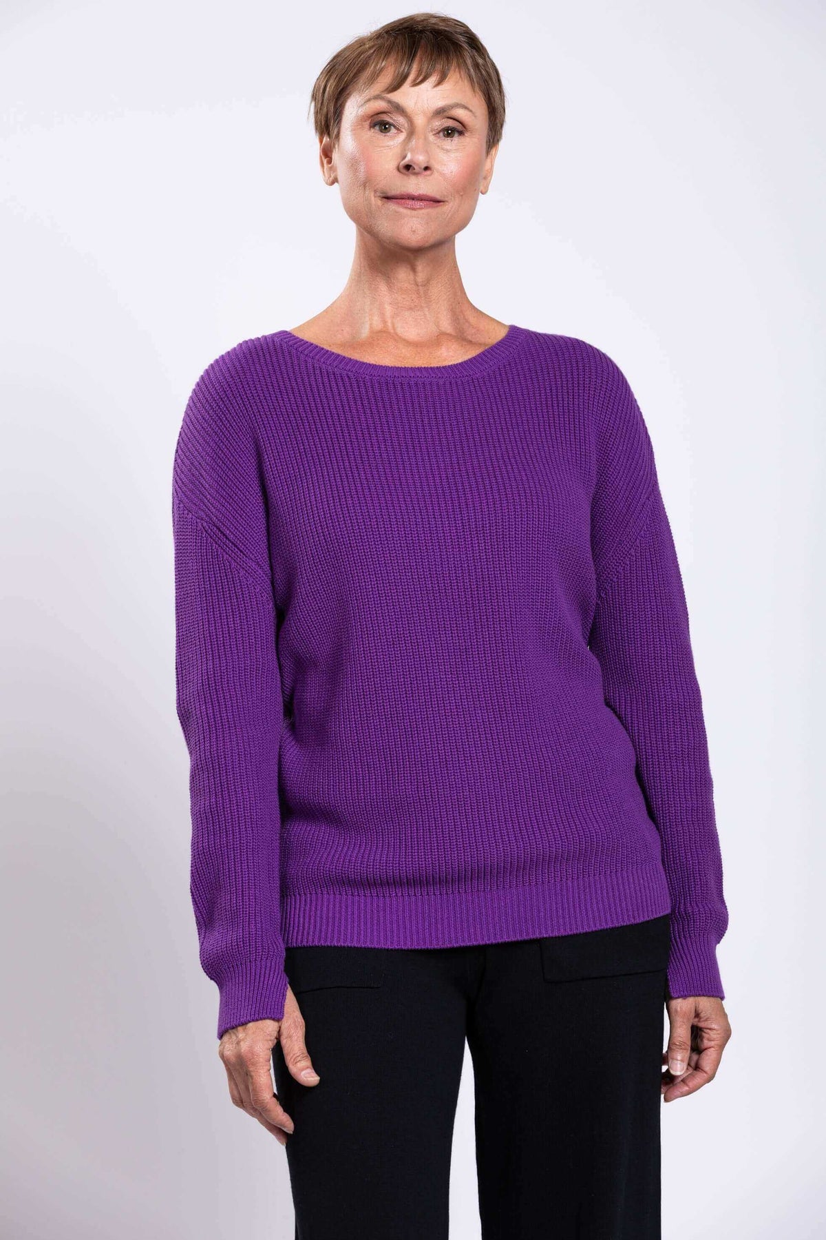 Woman wearing a relaxed fit purple shaker stitch cotton sweater with black pants