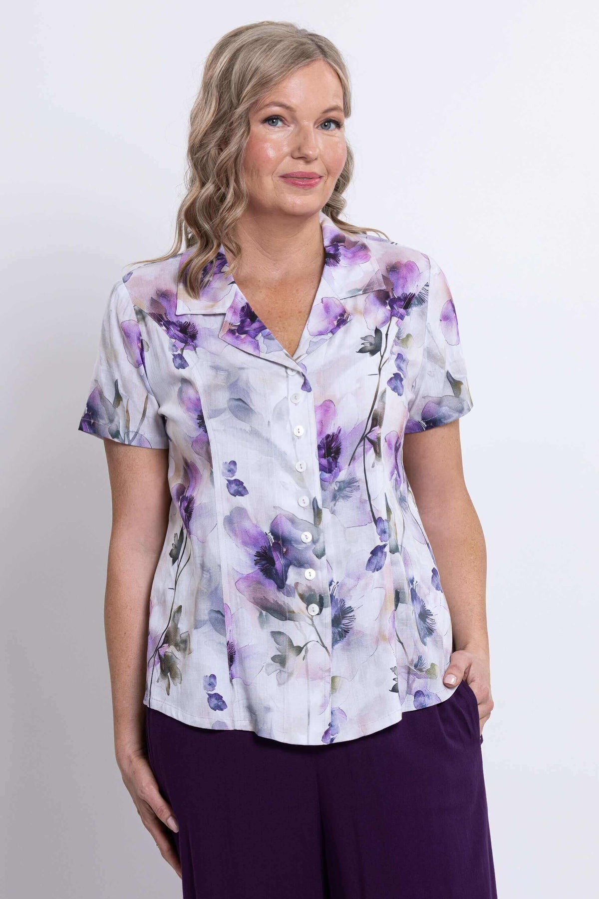 Woman wearing a short-sleeve floral blouse with purple flowers and button front, close view