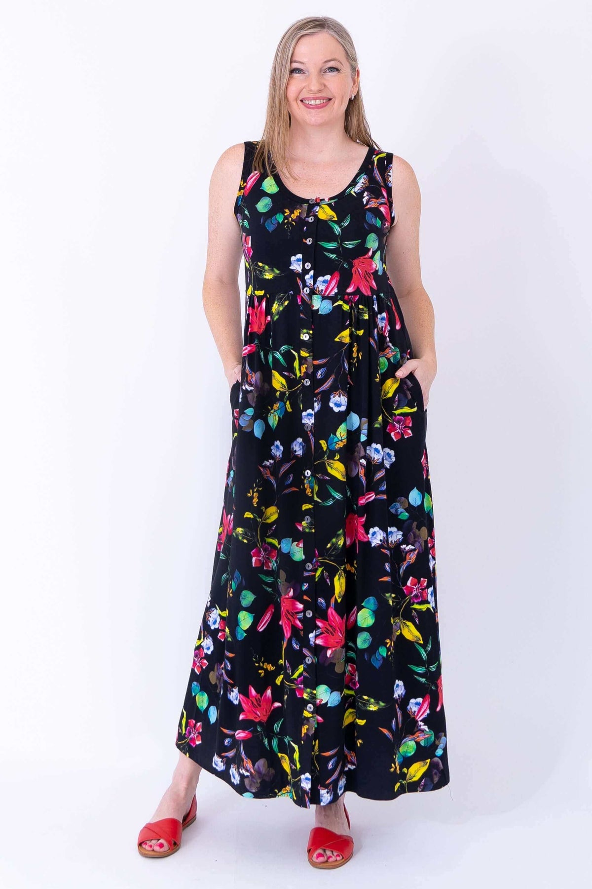 Woman wearing a sleeveless black maxi dress with colorful floral print and red sandals