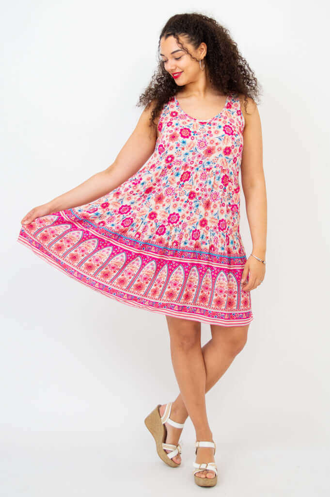 Woman wearing a sleeveless, pink and floral print scoop neck dress while holding the hem.