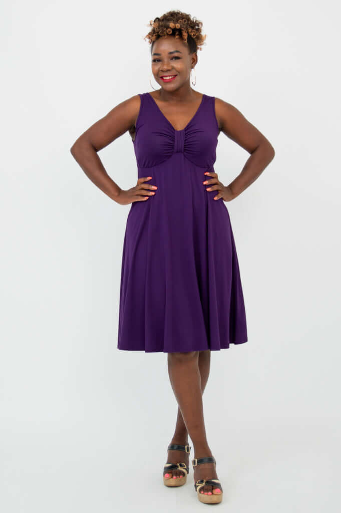 Woman wearing a sleeveless purple fit and flare dress, smiling confidently