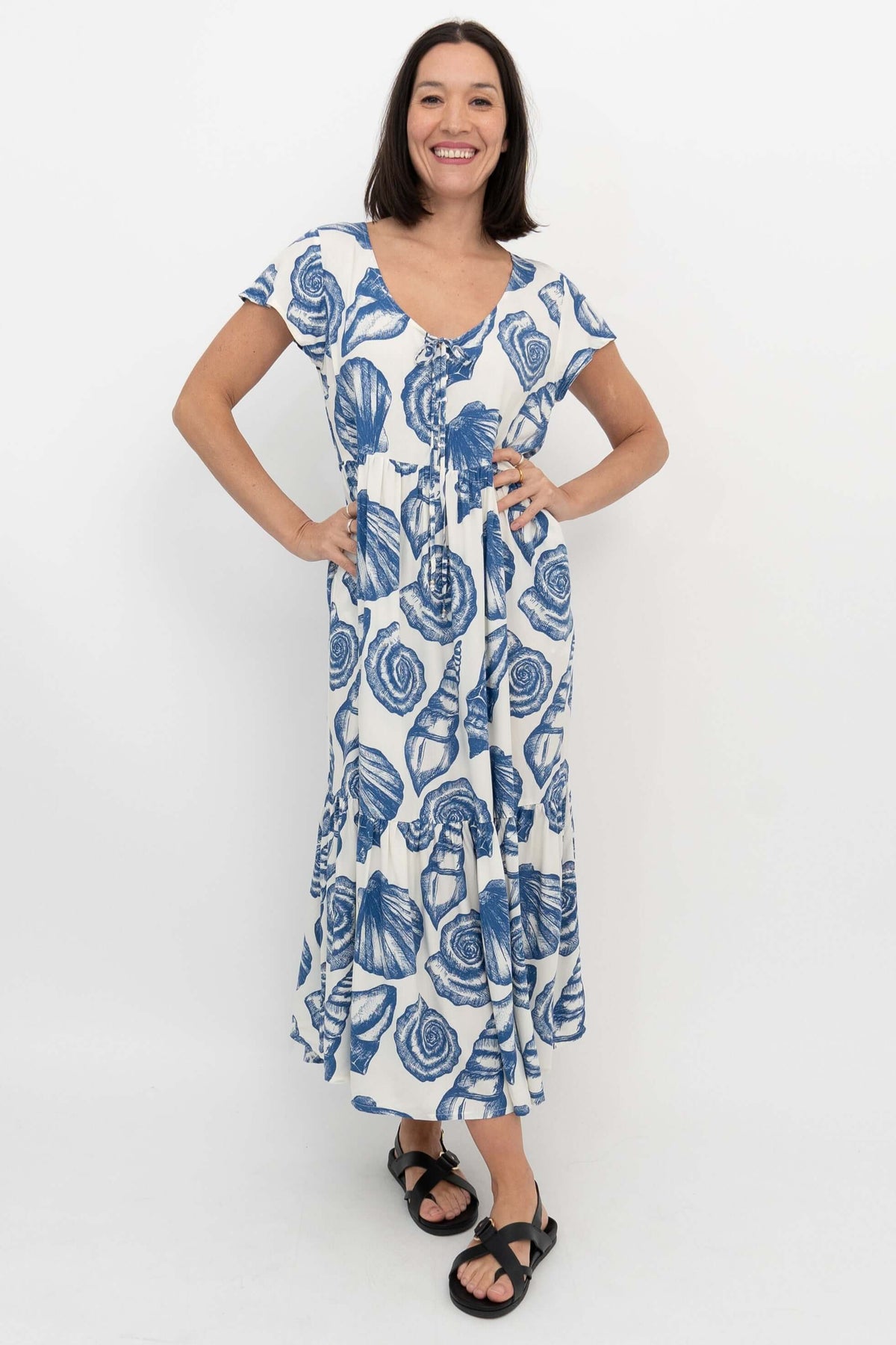 Woman wearing a white dress with blue seashell print, standing with hands on hips