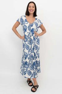 Woman wearing a white dress with blue seashell print, standing with hands on hips