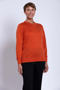Woman wearing an orange V-neck merino wool sweater with black pants