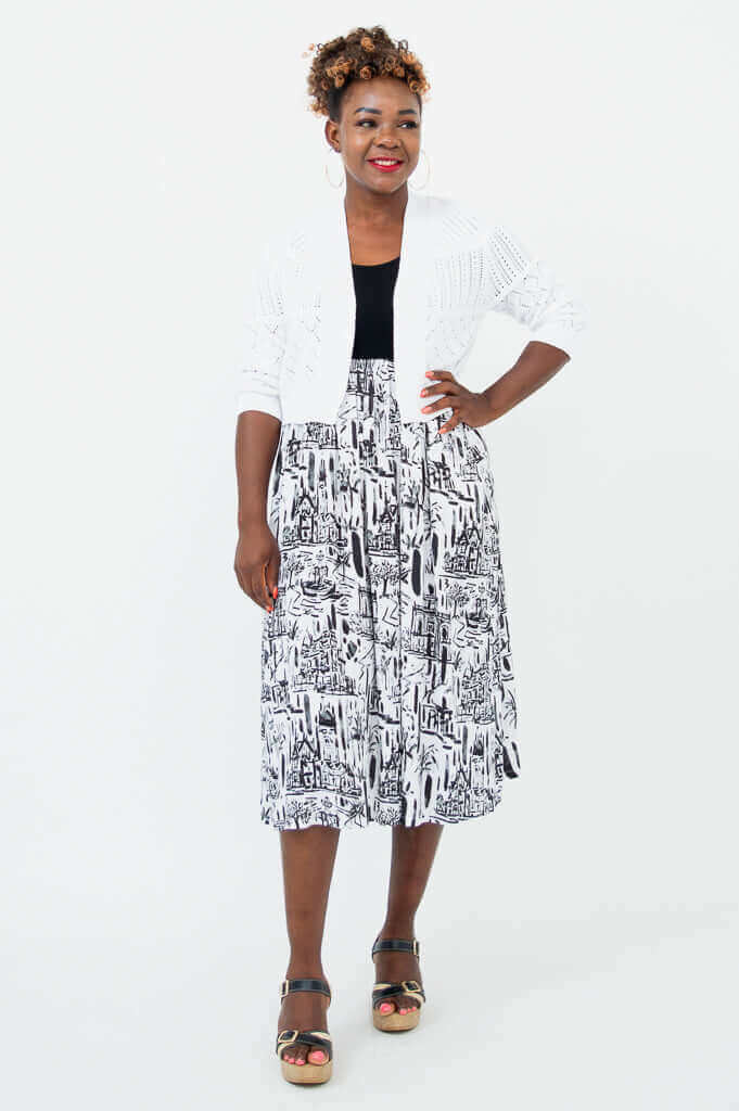 Woman in a black and white city print midi dress layered with a white knit cardigan