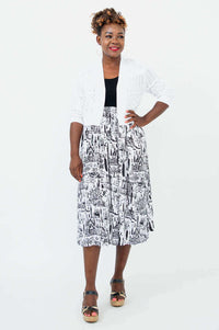 Woman in a black and white city print midi dress layered with a white knit cardigan