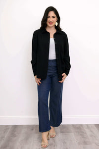 Woman wearing a black button-up shirt over a white top with blue wide-leg pants