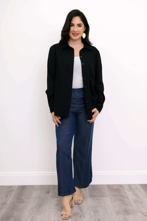Woman wearing a black button-up shirt over a white top with blue wide-leg pants