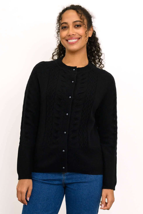Woman wearing a black cable knit cardigan with pearl buttons in a front view