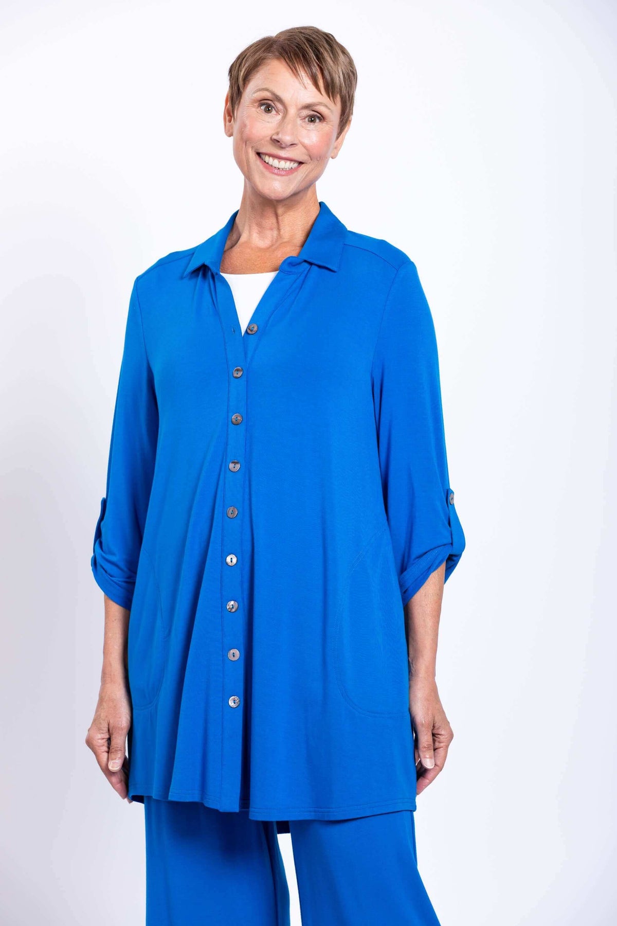 Woman wearing a bright blue button-up bamboo French terry blouse with rolled sleeves