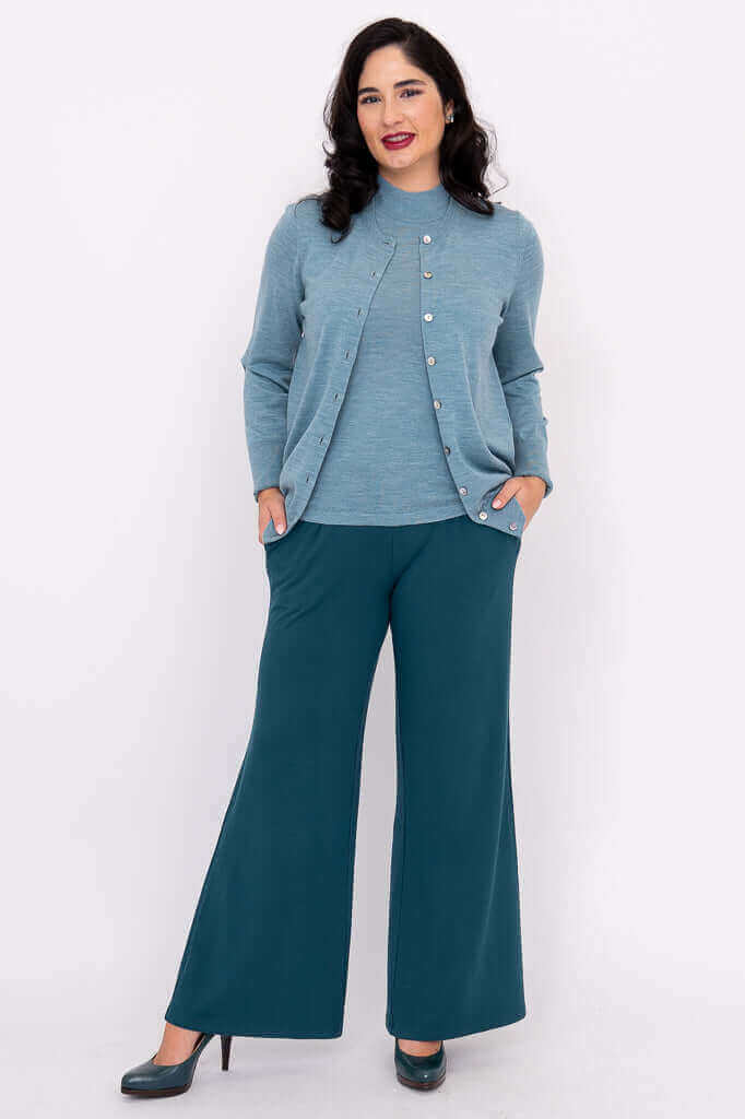 Woman wearing blue cardigan with hands in pockets and teal wide-leg pants