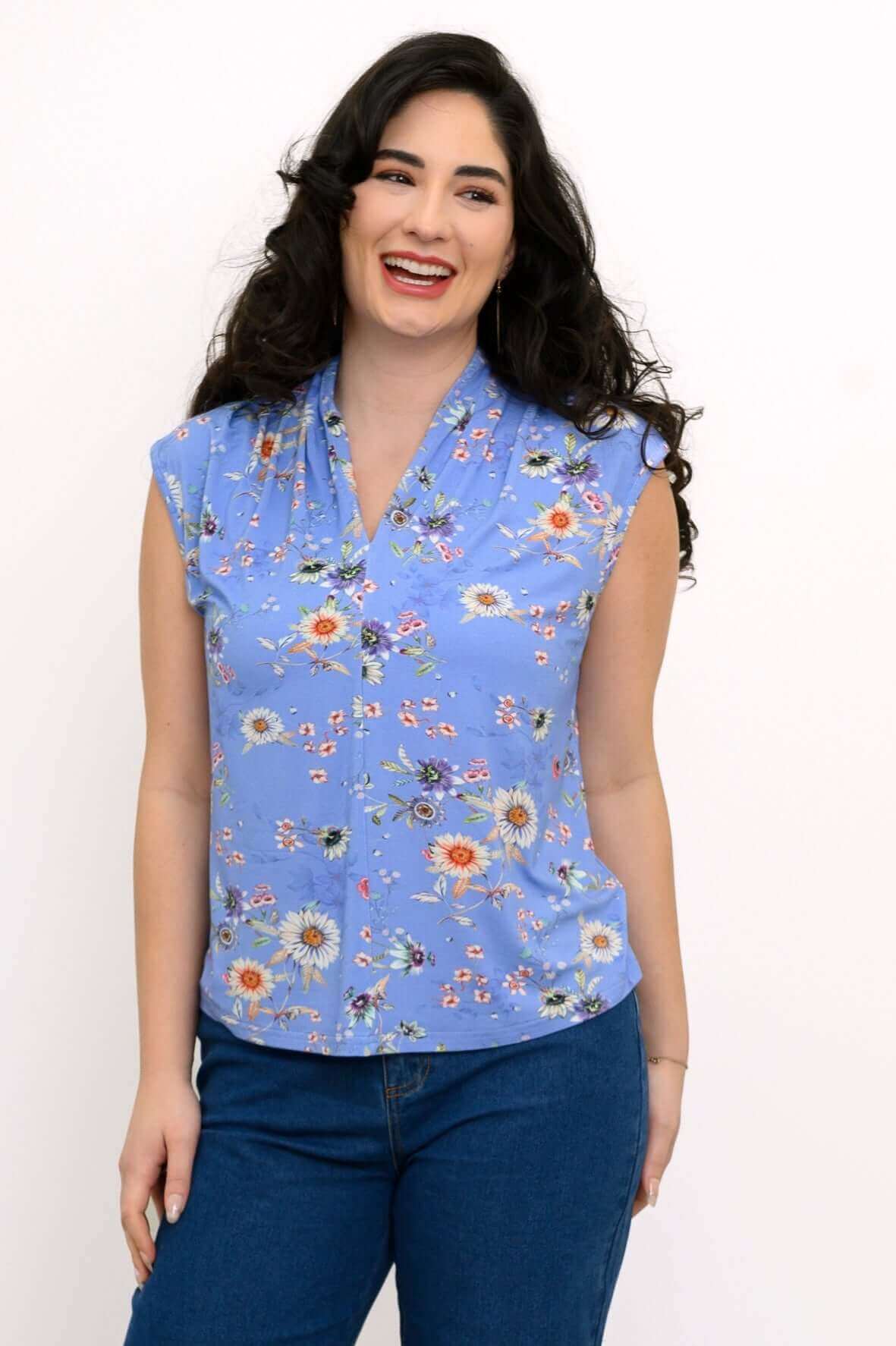 Woman wearing a blue sleeveless floral top with v-neck and shawl collar, smiling