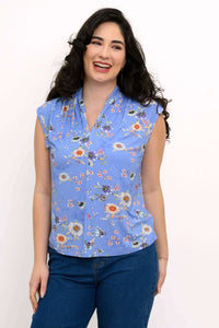 Woman wearing a blue sleeveless floral top with v-neck and shawl collar, smiling