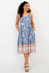 Woman in blue floral dress with hands in pockets, smiling