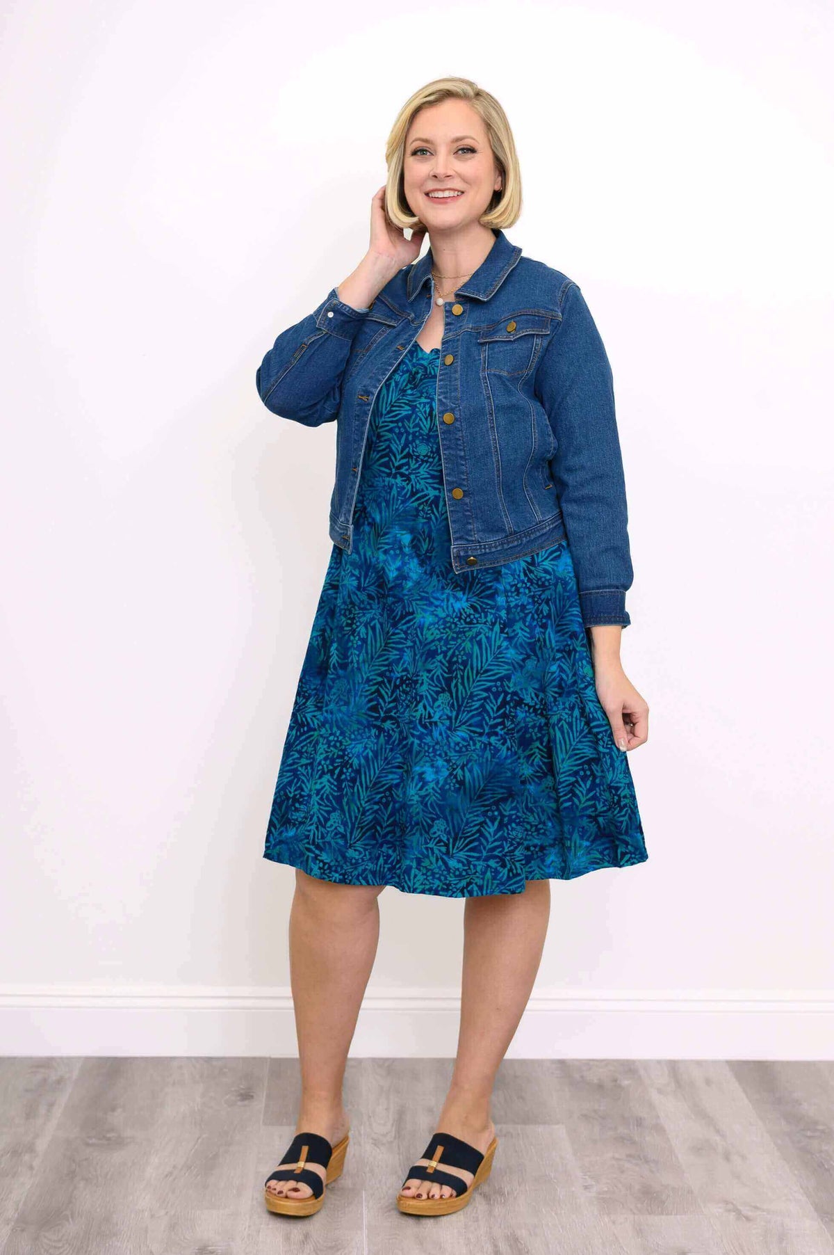 Woman styling blue tropical leaf dress with a denim jacket and sandals