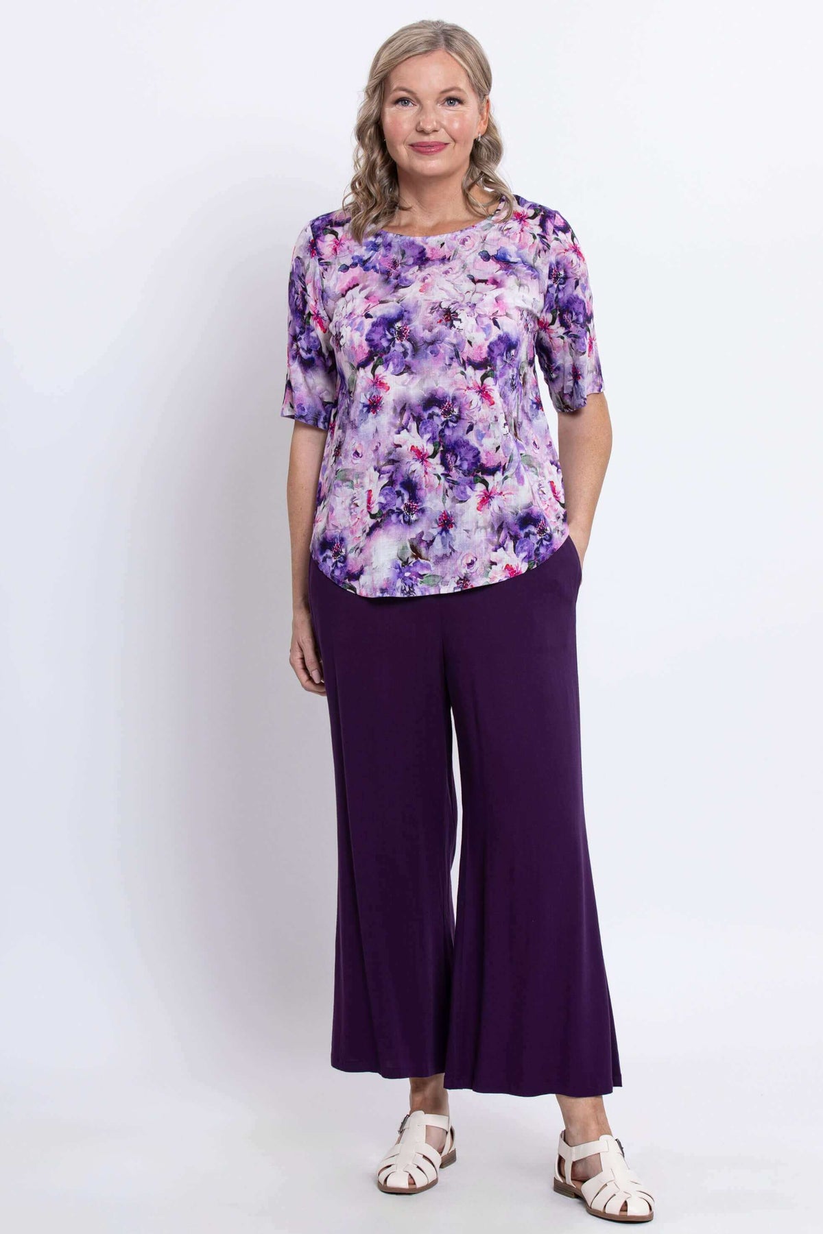 Woman modeling a scoop neck floral blouse and purple pants, standing forward