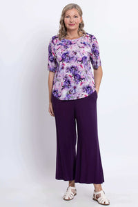 Woman modeling a scoop neck floral blouse and purple pants, standing forward