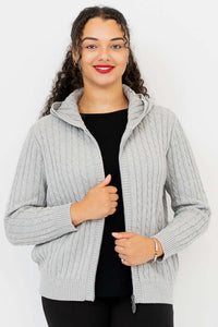Woman wearing a light grey cable knit zip-up hoodie with a hood, hand on zipper