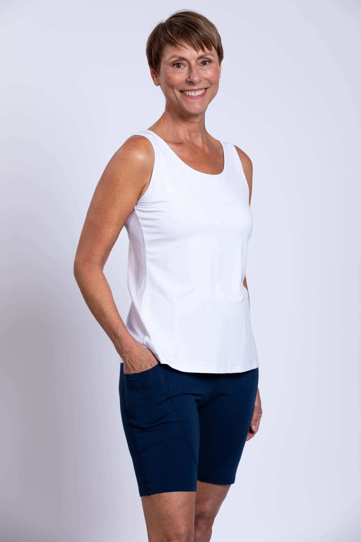 Woman wearing navy Robson Shorts and white sleeveless top, smiling, with hand in pocket