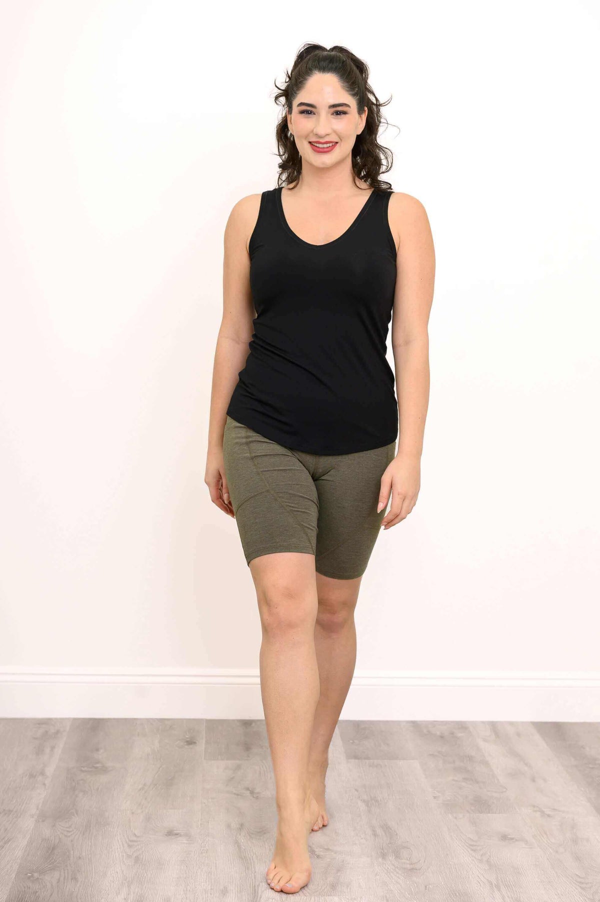 Woman wearing olive green stretch shorts and black tank top, standing barefoot