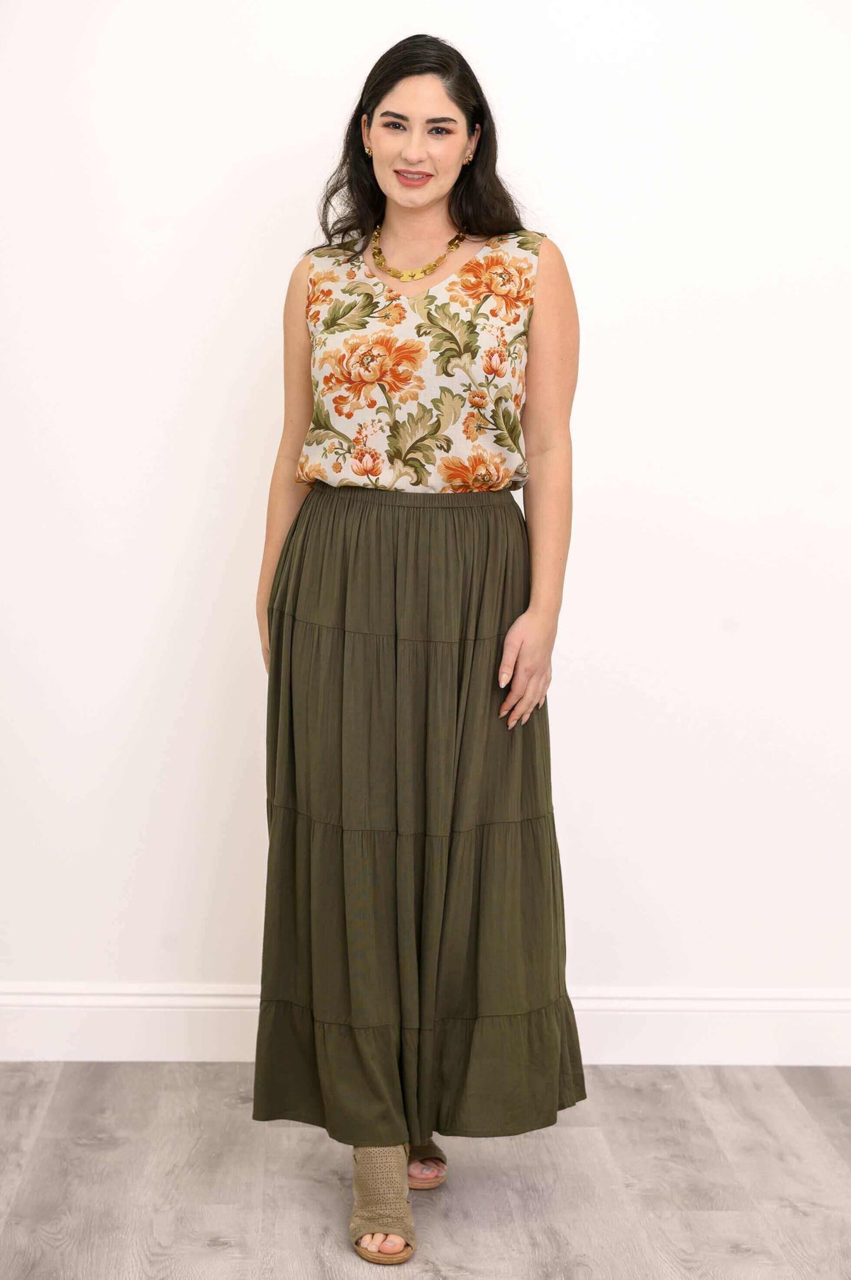 Woman wearing an olive green tiered maxi skirt and floral top standing indoors