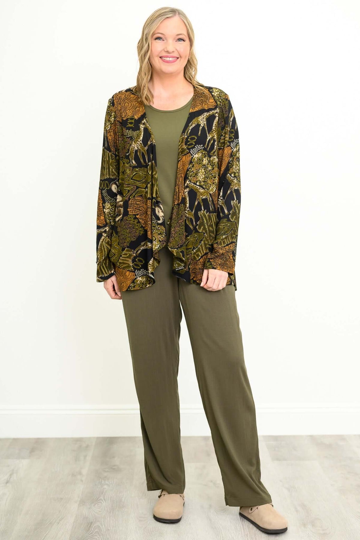 Woman wearing matching olive green pants, shirt, and patterned jacket, smiling