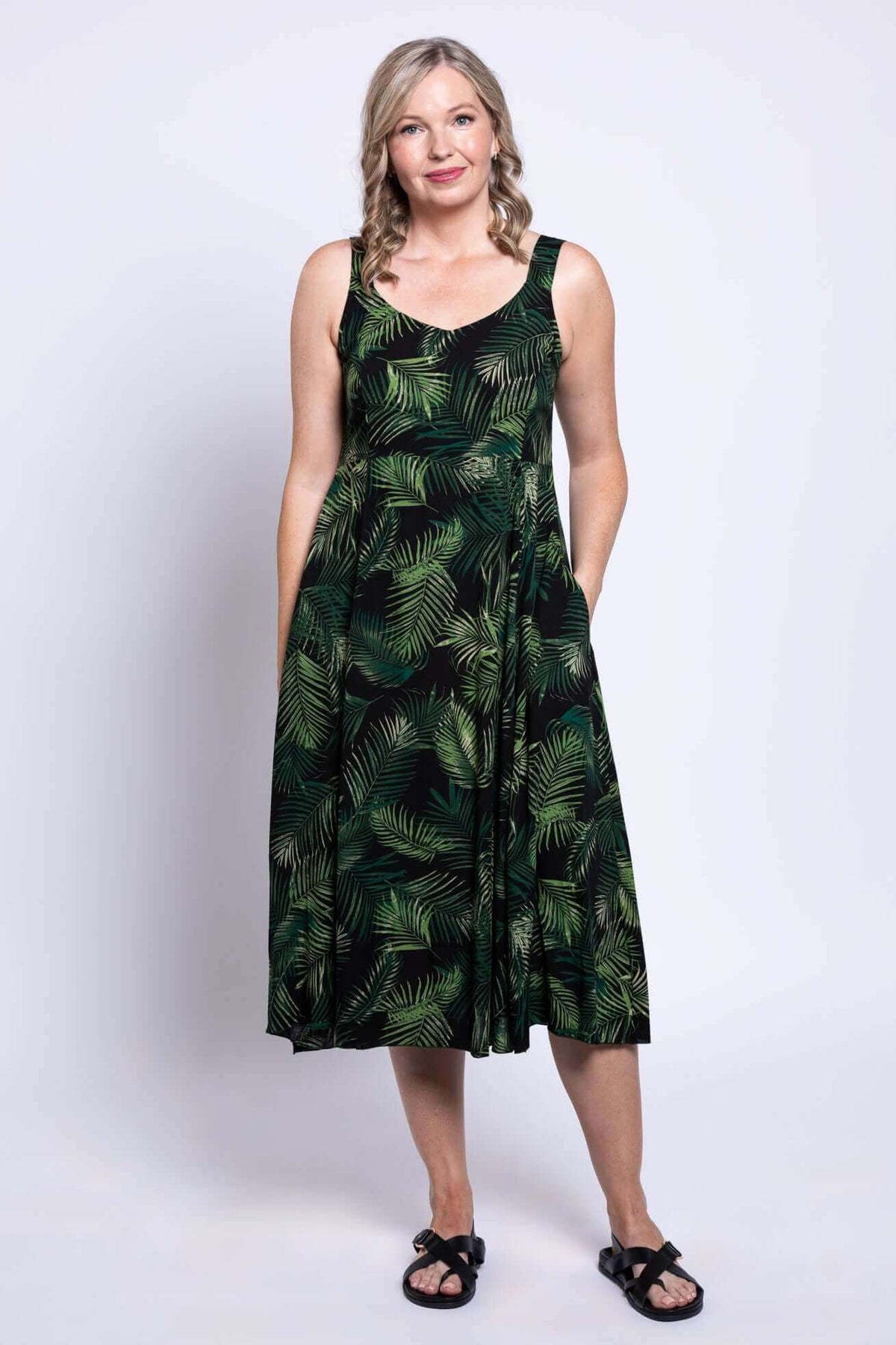Woman wearing a sleeveless black dress with green leaf print and pockets