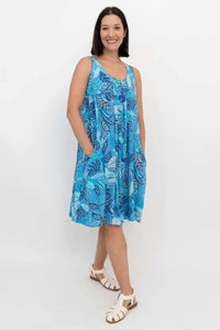 Woman wearing sleeveless blue leaf print dress, standing and smiling